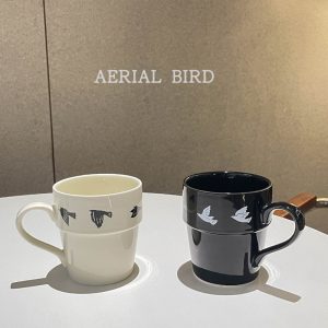 Hand carrying a ceramic mug with a bird motif